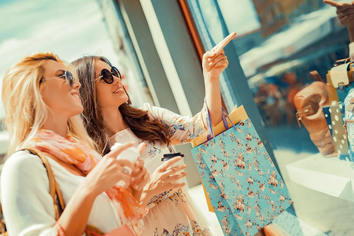 Dos mujeres sonrientes con bolsas de compras buscando regalos en una tienda.