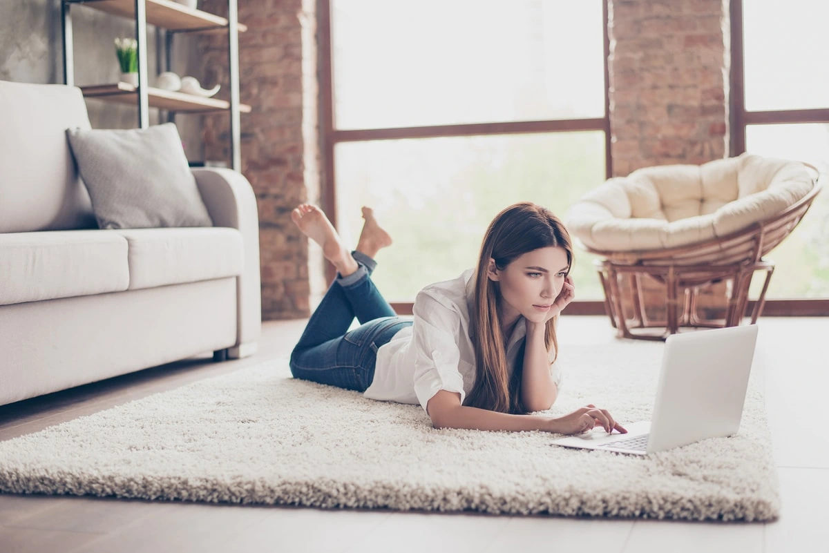 Mujer acostada revisando perfiles en redes sociales desde su computadora portátil.
