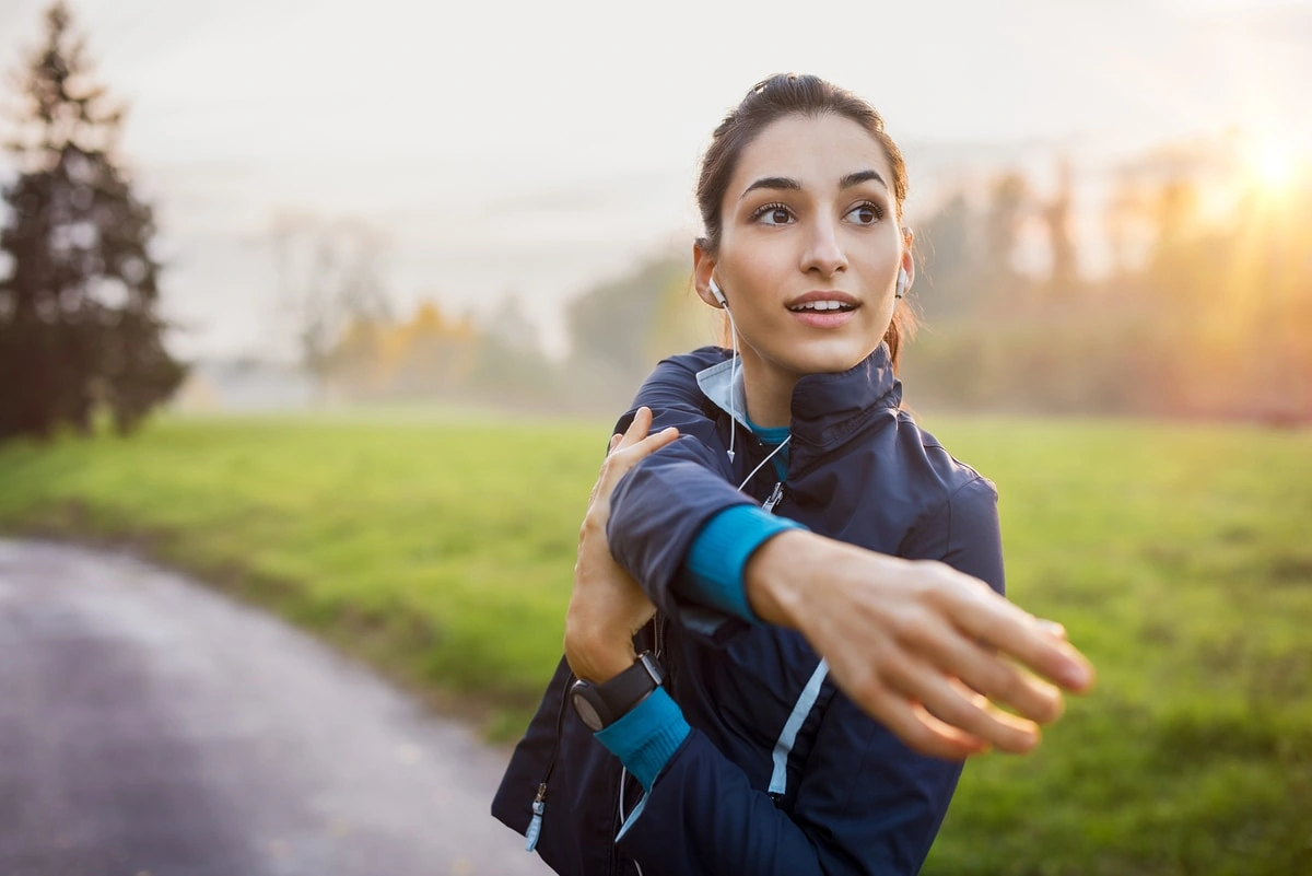 Mujer joven haciendo estiramientos al aire libre con auriculares mientras se prepara para correr al amanecer.
