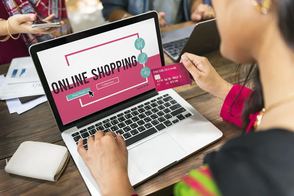 Mujer joven comprando en línea en su laptop con su tarjeta de crédito en la mano