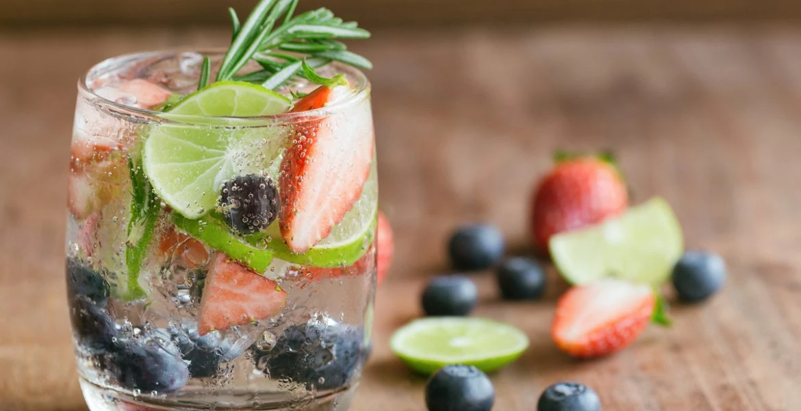 Vaso de una refrescante agua saborizada casera, infusionada con frutas frescas como fresas, arándanos y rodajas de limón.