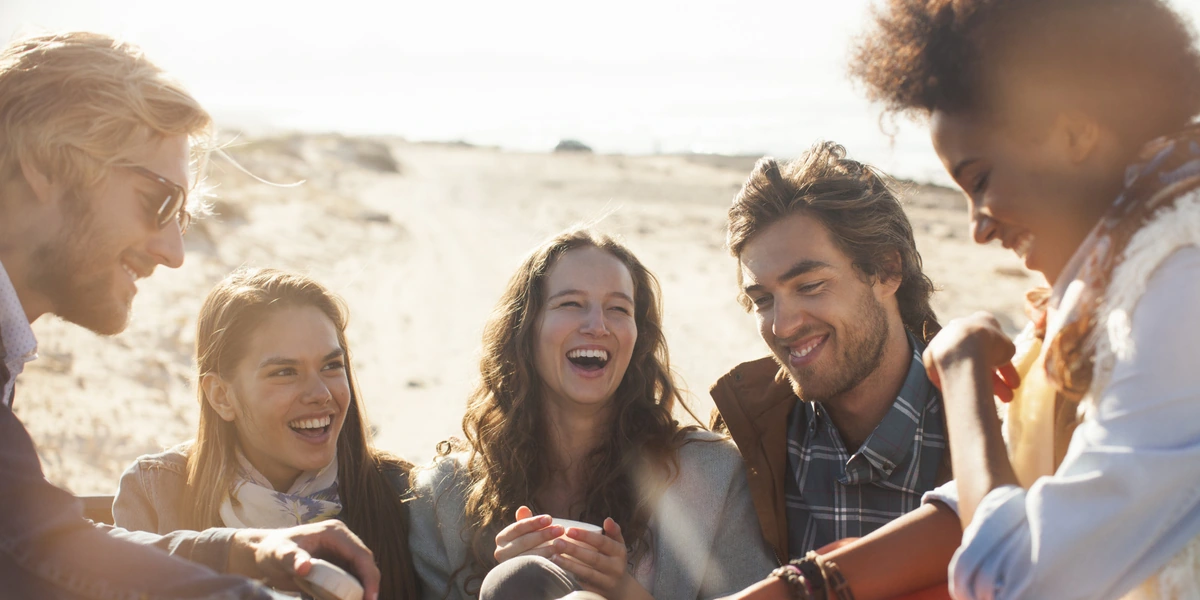 Grupo de amigos jóvenes riendo y disfrutando juntos en la playa, simbolizando la felicidad de recuperar la amistad tras perdonar y dejar ir el rencor.