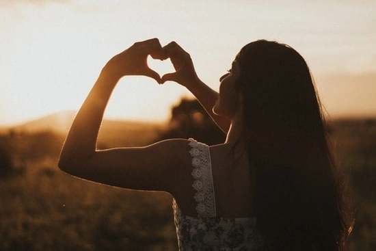 Mujer romántica haciendo un corazón con sus manos hacia el horizonte.