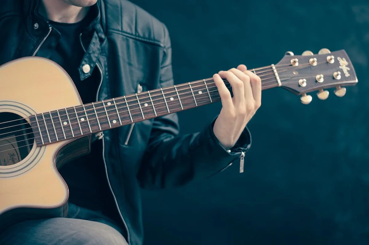 Un hombre practica guitarra mientras sigue una clase en línea desde una tablet, usando una app pensada para principiantes.