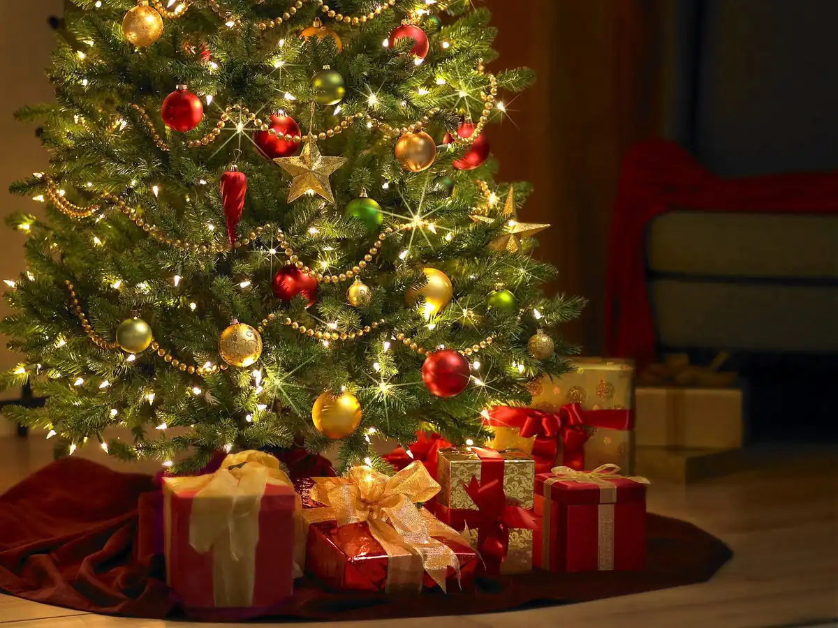 Pino de Navidad decorado con bolas grandes, guirnaldas doradas y luces, con grandes paquetes y regalos a sus pies.