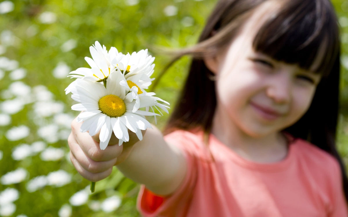 Niña ofreciendo flores en un campo, disfrutando de la naturaleza.