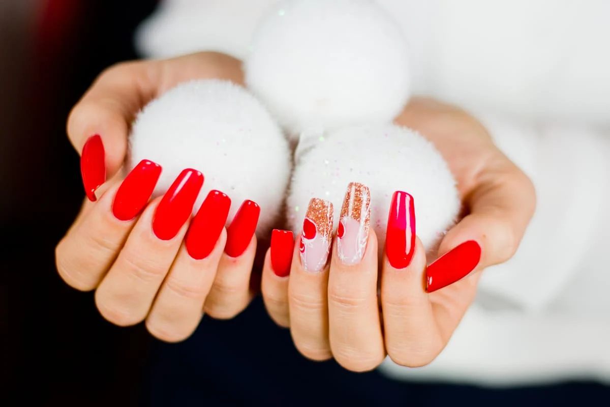 Manos con uñas largas pintadas de rojo, una con diseño dorado, sosteniendo pompones blancos