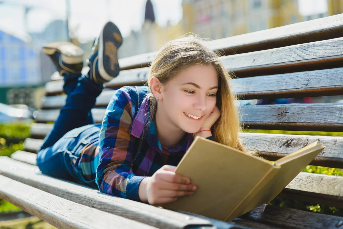 Mujer joven leyendo un libro con expresión de felicidad y disfrute.