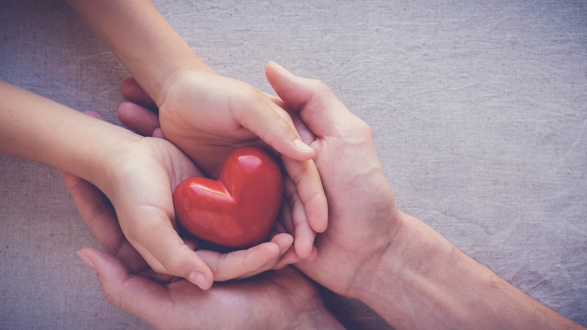 Manos de un adulto sosteniendo las manos de un niño, con un corazón de cerámica en ellas.