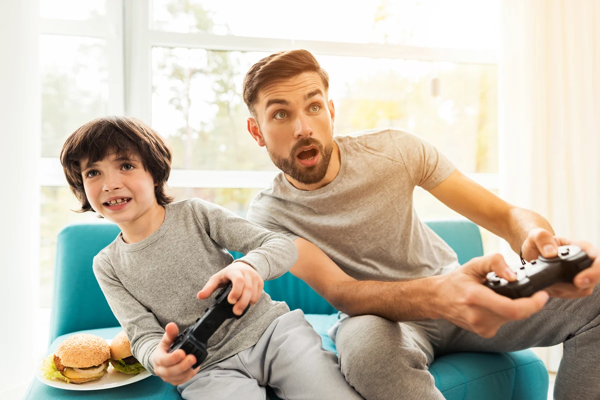 Padre e hijo jugando videojuegos con entusiasmo, una idea de regalo perfecta para un papá 'gamer' en el Día del Padre.