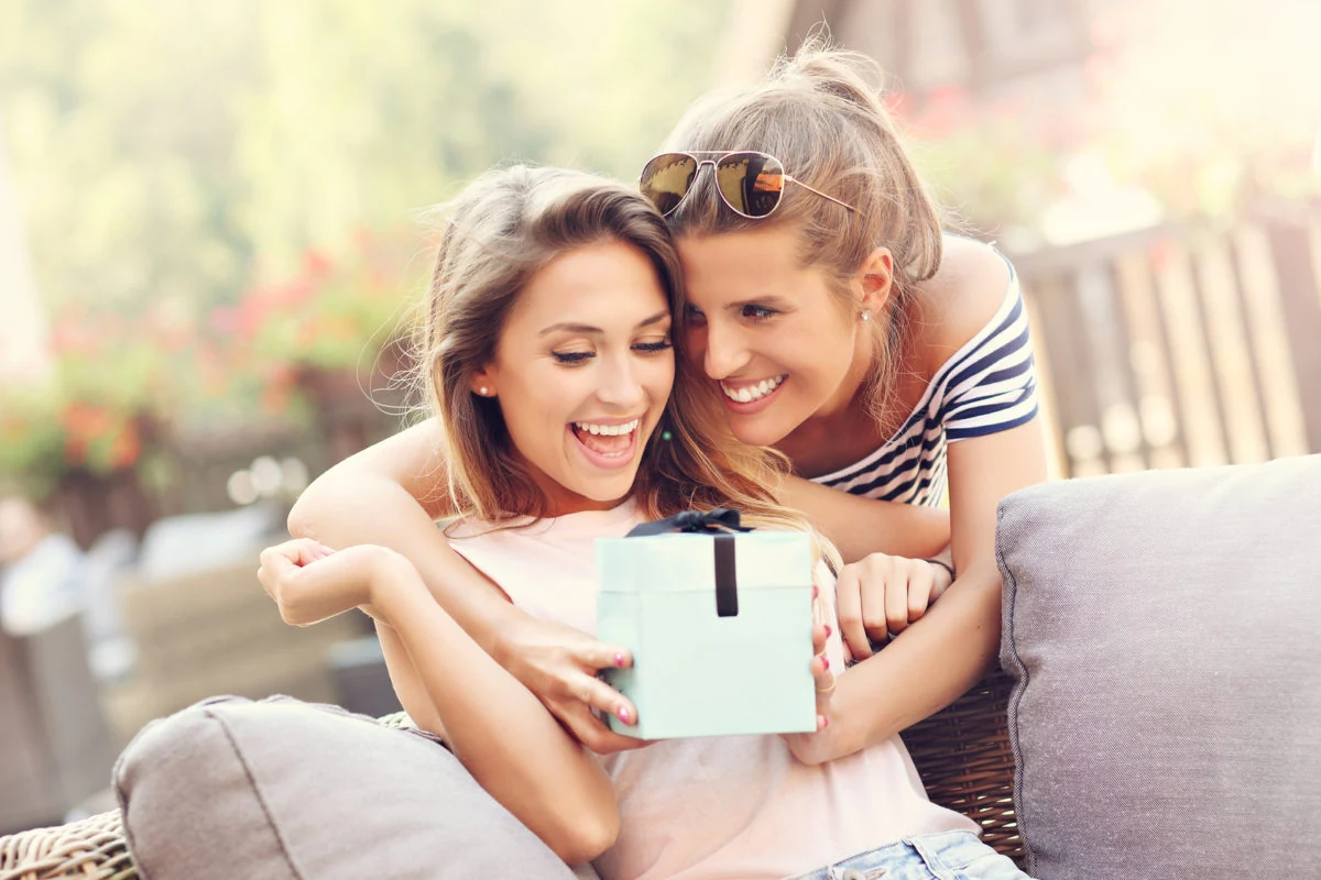 dos amigas sonrientes abriendo un regalo en exteriores