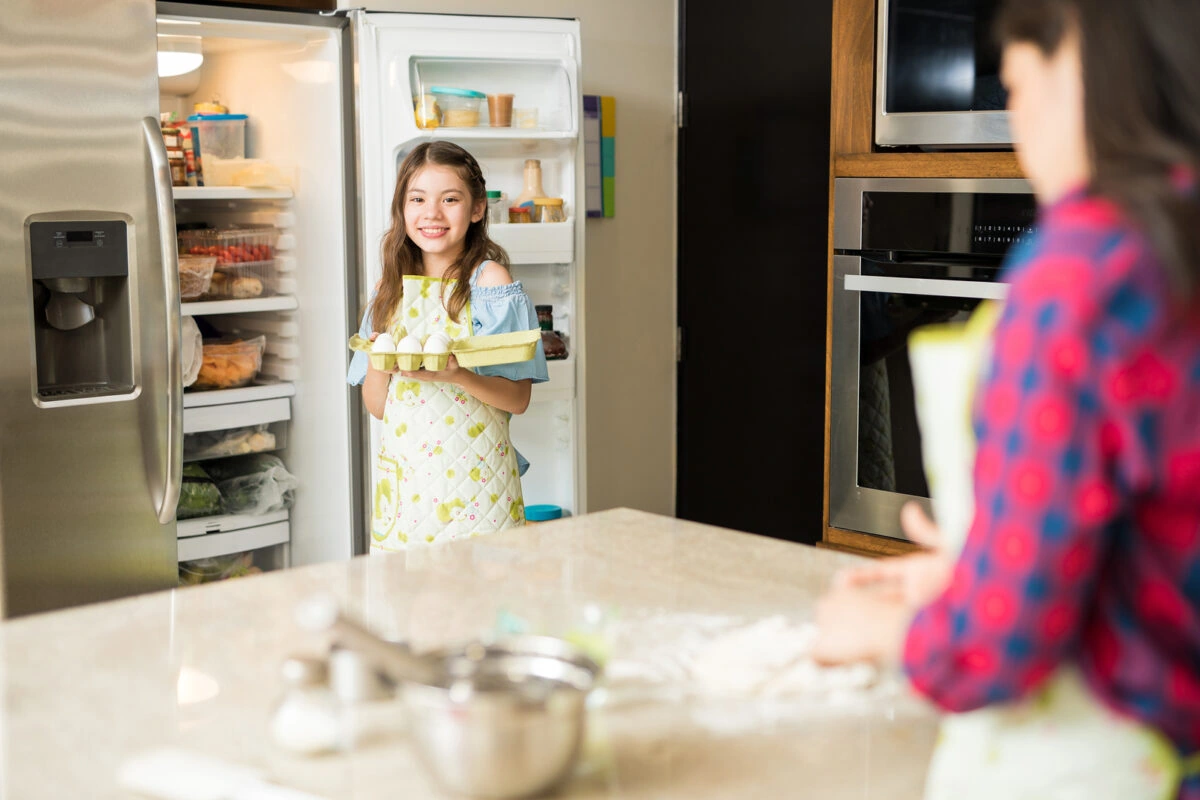 Niña sonriente sacando huevos del refrigerador en la cocina de su casa