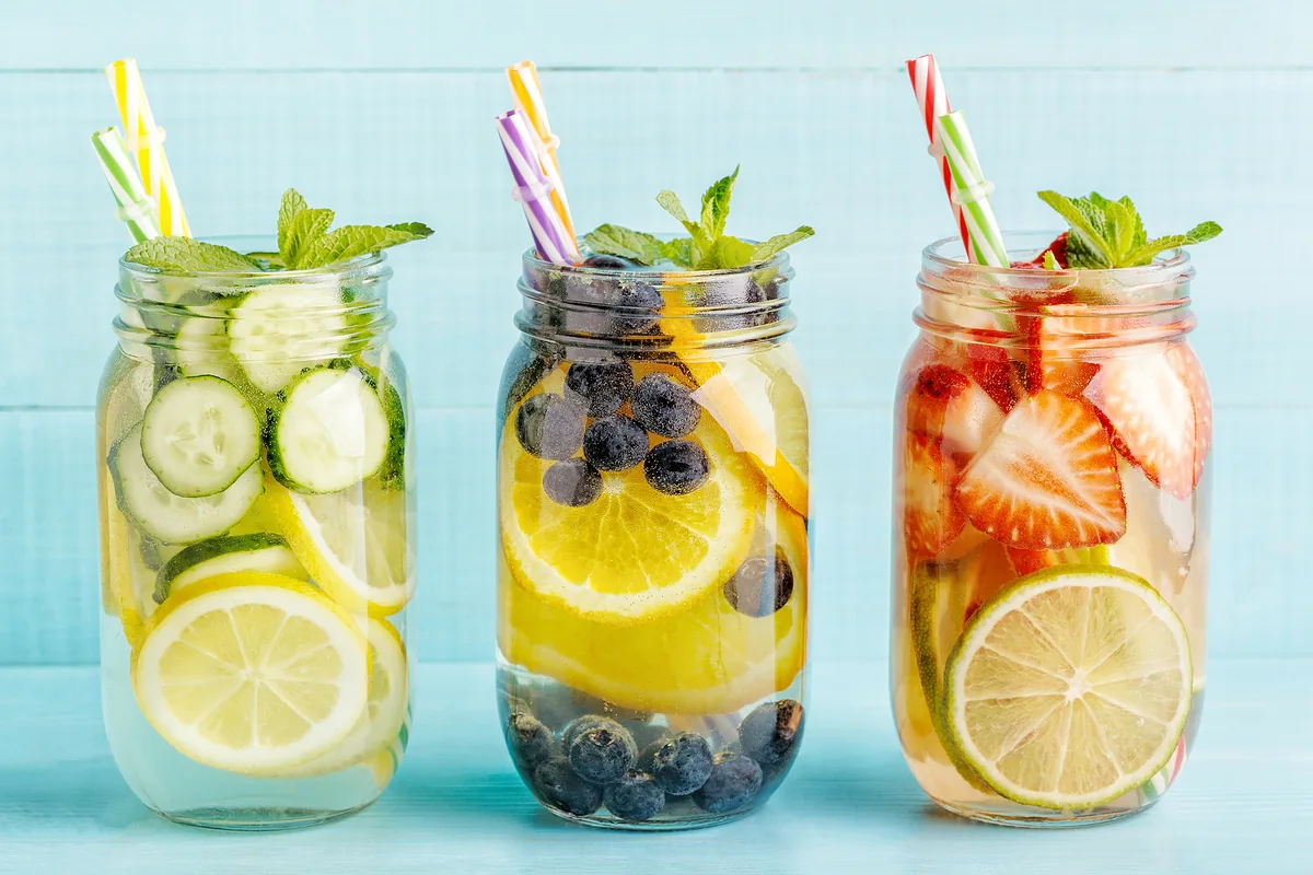 Tres variedades de aguas saborizadas caseras en jarras de vidrio, mostrando combinaciones con limón y pepino, naranja y arándanos, y fresa con lima.