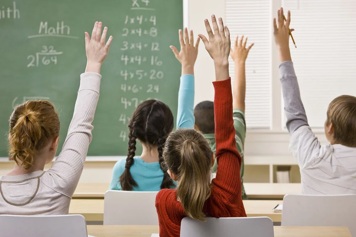 Frases para maestros: alumnos levantan la mano en salón de clases