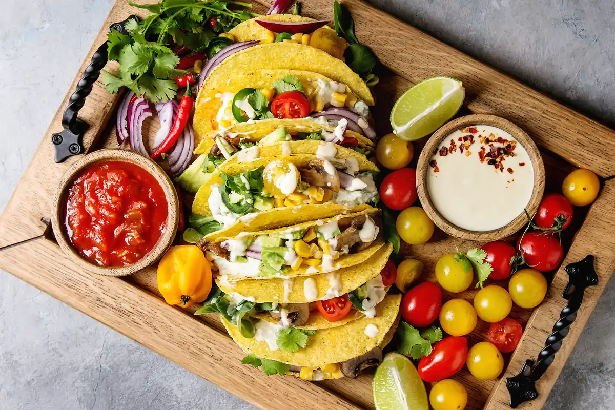 Tacos de maíz rellenos con verduras, salsa, lima y tomates cherry sobre una tabla de madera
