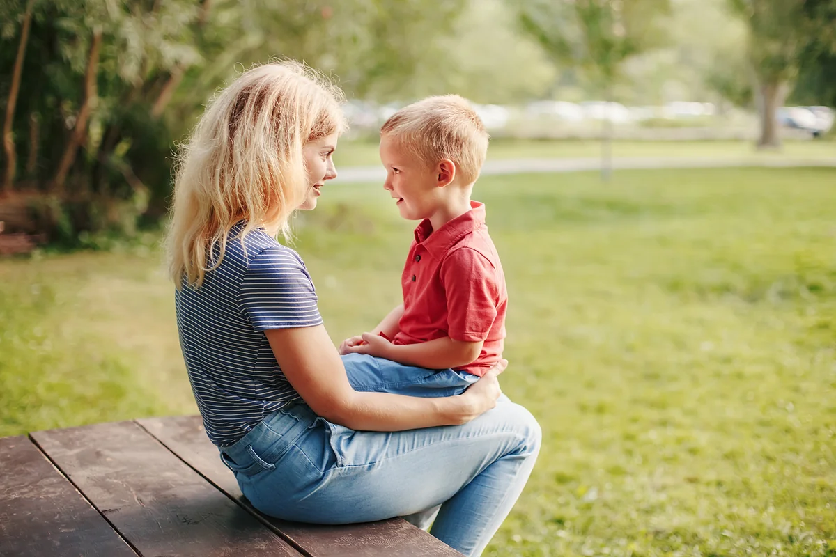 Madre e hijo sentados frente a frente en un parque, conversando con ternura.