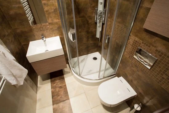Diseño de baño pequeño con cabina de ducha esquinera y mampara o cancel de vidrio transparente para maximizar el espacio visual y la funcionalidad.