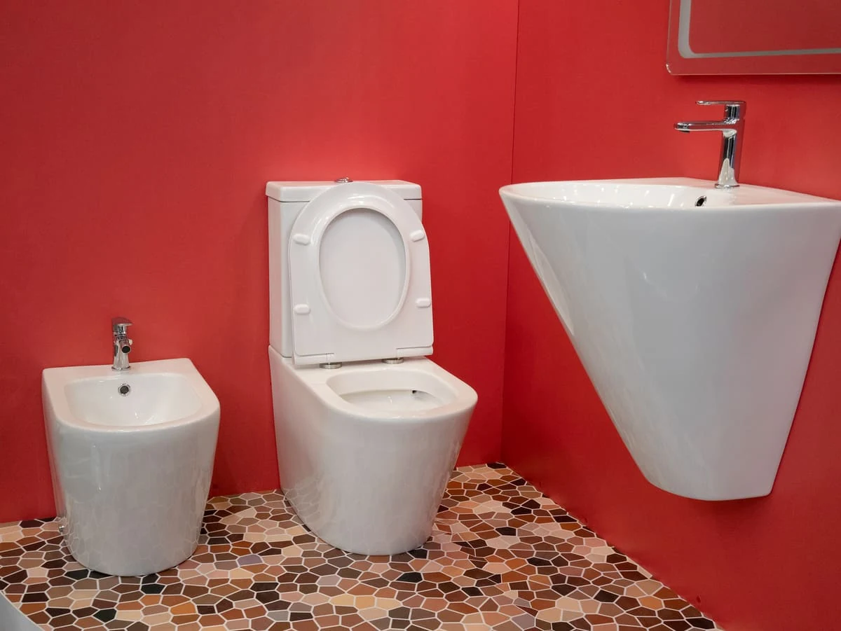 Diseño de baño atrevido con paredes color rojo intenso, sanitarios blancos suspendidos y suelo de mosaico de piedras en tonos tierra para crear contraste y personalidad.