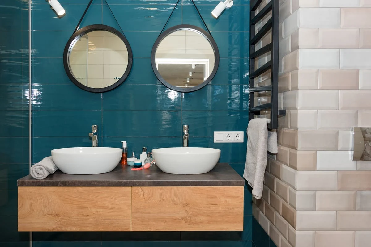 Decoración de baño pequeño con azulejos en color azul petróleo brillante, mueble de madera y revestimiento tipo ladrillo blanco para ganar luminosidad.