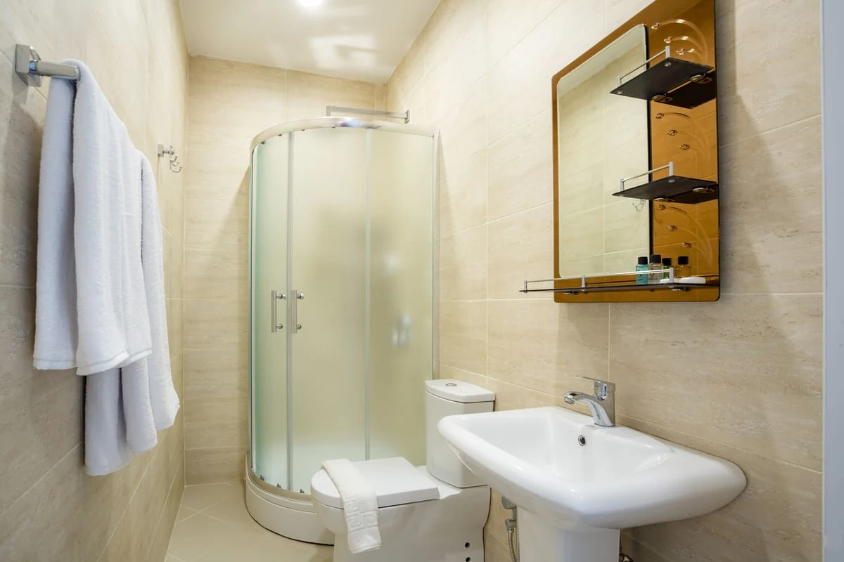 Diseño de baño pequeño revestido con azulejos color beige y crema, con cabina de ducha y accesorios blancos para crear una sensación de amplitud y luminosidad.