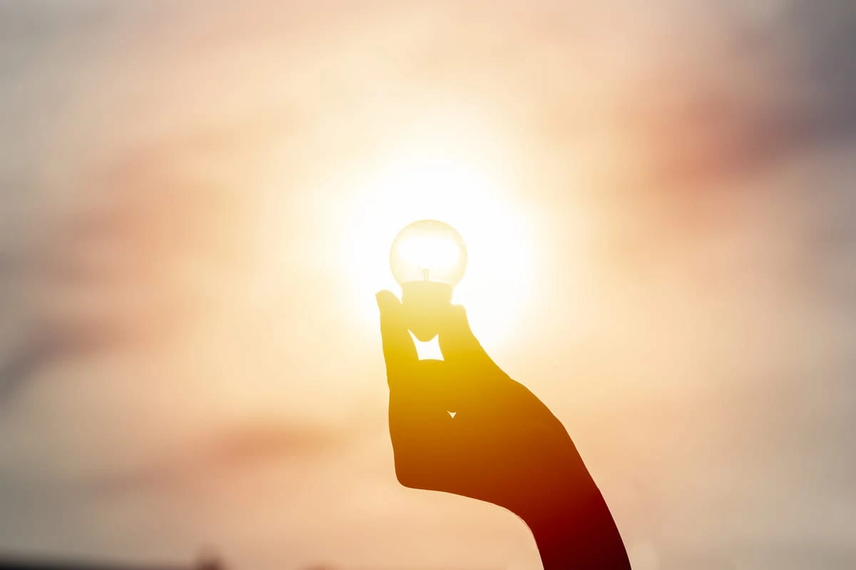 Mano sostiene una bombilla iluminada por el sol, símbolo de energía solar y sostenibilidad.