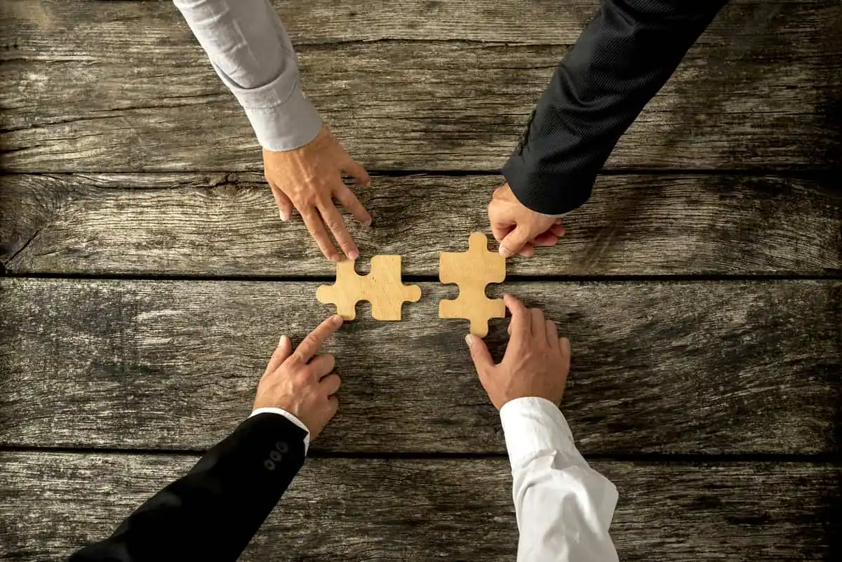 Colaboración y Solución en Equipo Un equipo de trabajo colaborando para conectar dos piezas de rompecabezas, simbolizando la solución de problemas y el liderazgo efectivo.