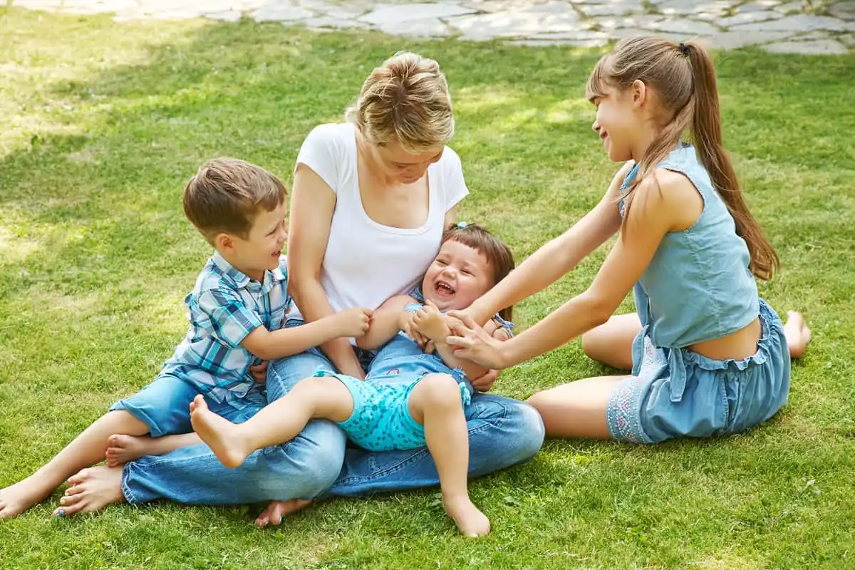 Madre jugando en el césped con sus tres hijos, símbolo de unión familiar y amor entre hermanos.