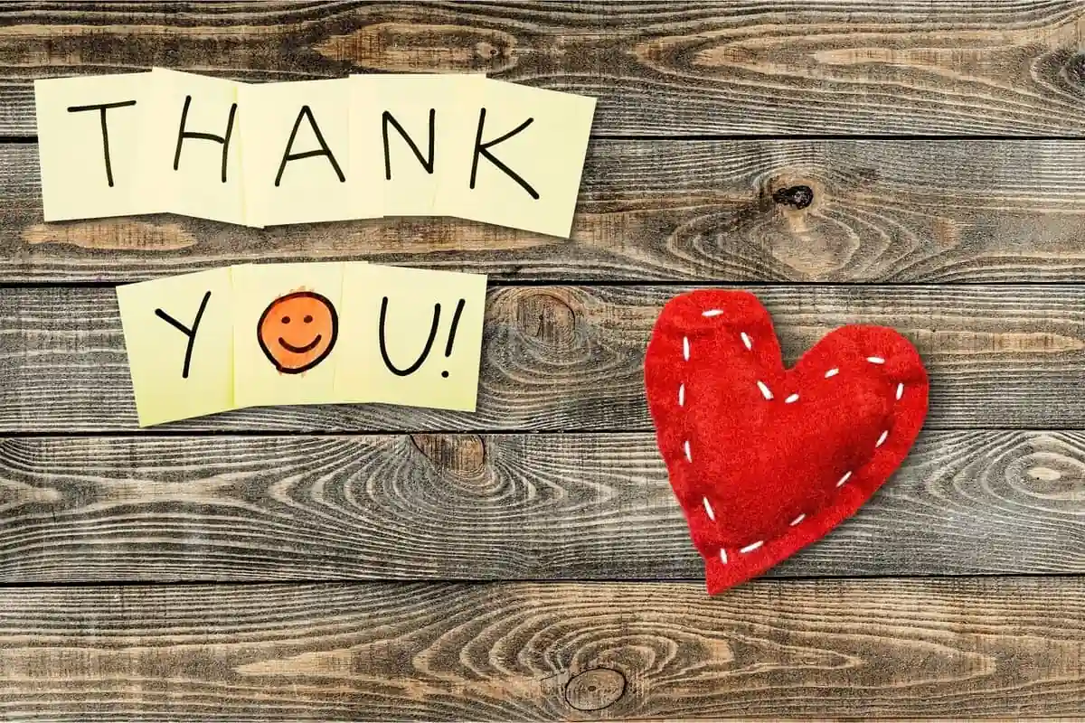 Cartel con las palabras Thank you sobre una mesa de madera con un corazón de tela rojo