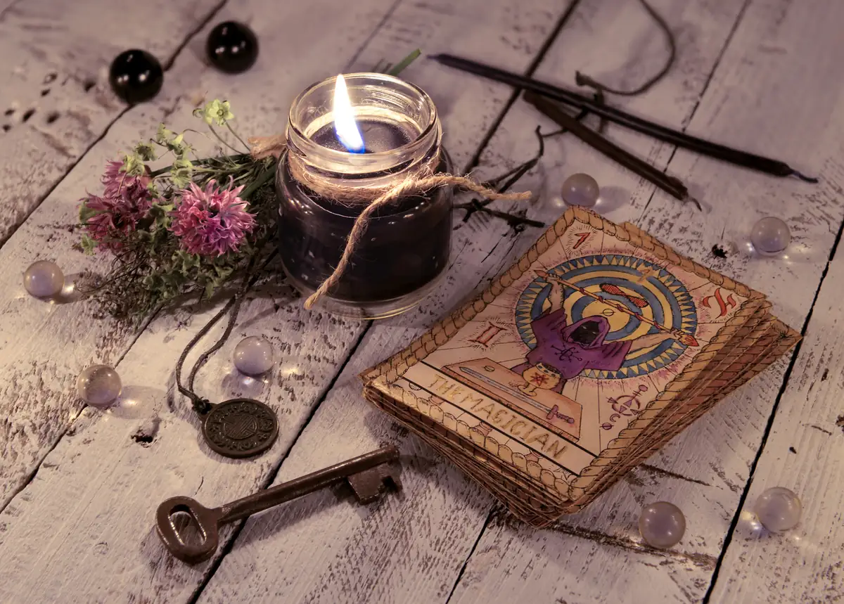 Escena mística con una vela encendida, cartas de tarot, llave antigua y elementos esotéricos sobre una mesa de madera clara.
