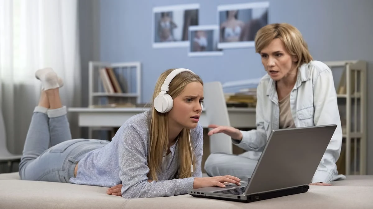 Madre y adolescente conversando mientras usan una computadora portátil, en un entorno hogareño.