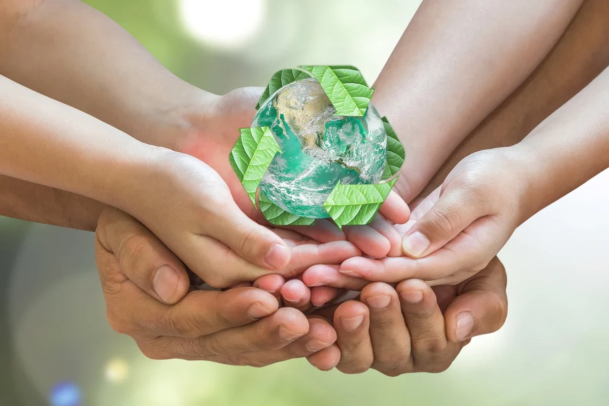 Varias manos sostienen una figura del planeta Tierra rodeada de hojas verdes, representando el cuidado del medio ambiente.
