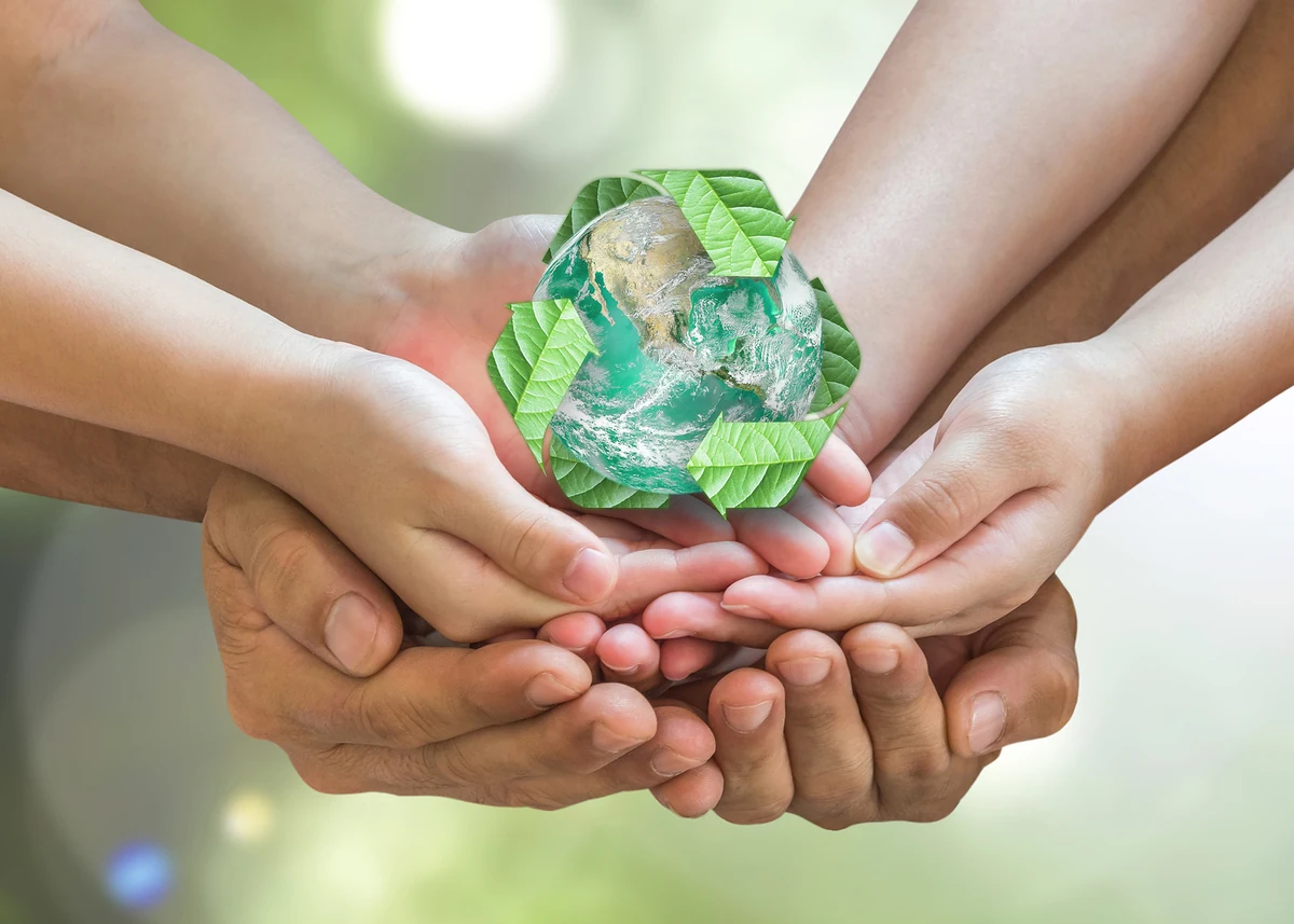Energías renovables: un compromiso global para proteger el planeta. Varias manos sostienen una figura del planeta Tierra rodeada de hojas verdes, representando el cuidado del medio ambiente.