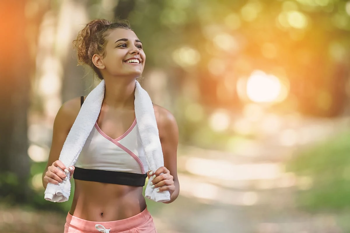 Joven entrenando en un parque, con top deportivo, calzas y toalla en el cuello