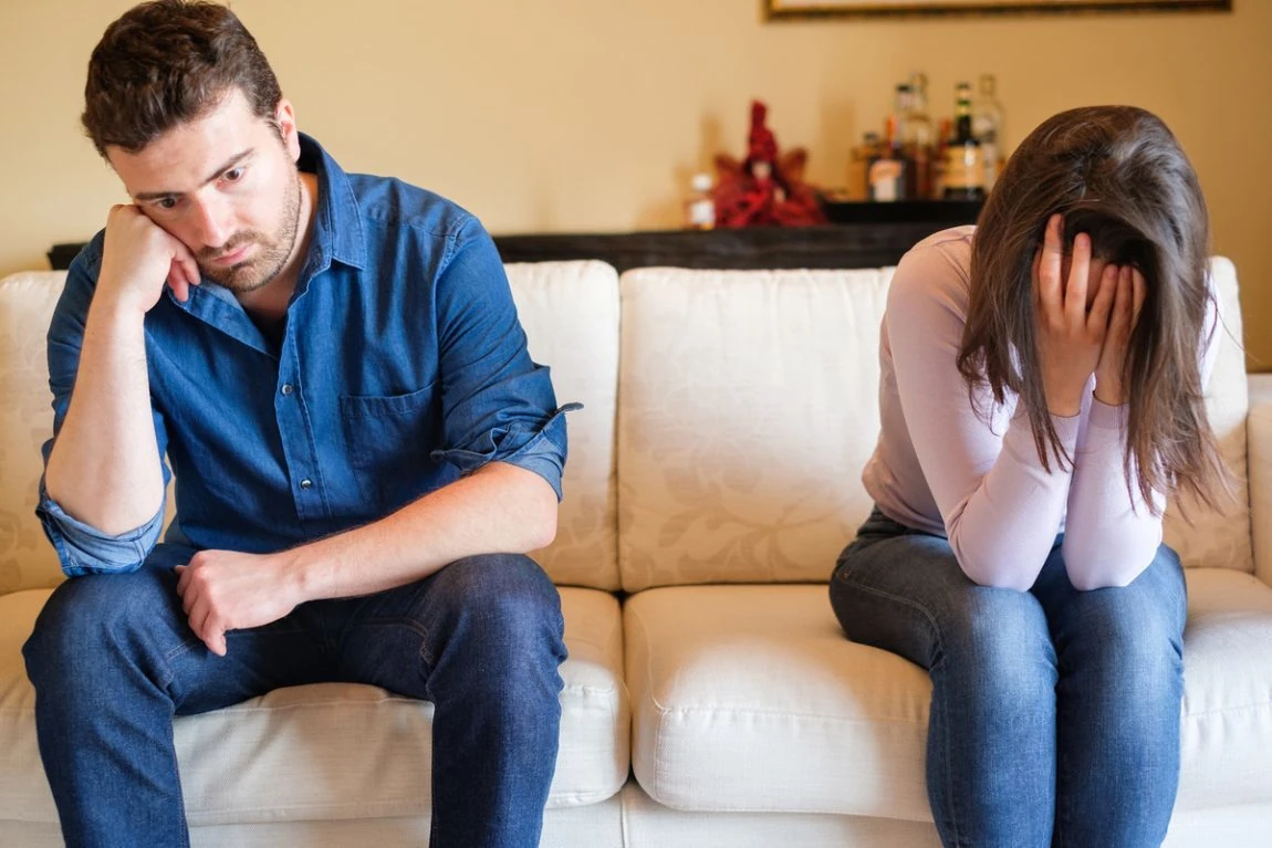 Pareja con problemas sentimentales sentada en un sofá, mostrando tristeza y distanciamiento.