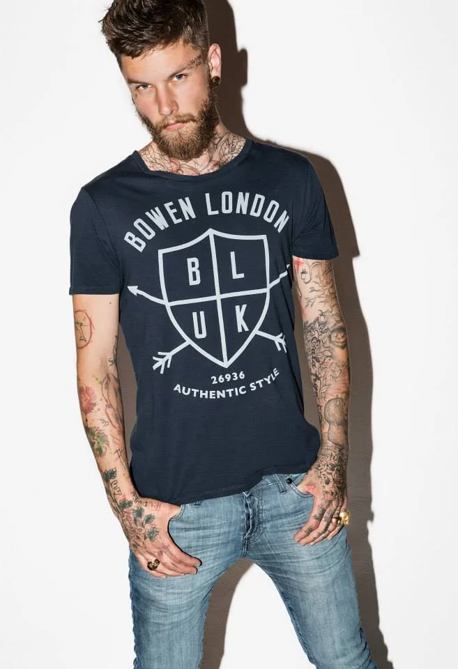 Tu Lienzo de Estilo Personal. Hombre con barba y tatuajes vistiendo una camiseta con estampado gráfico (graphic tee), un básico esencial en la ropa de hombre para expresar un estilo auténtico.