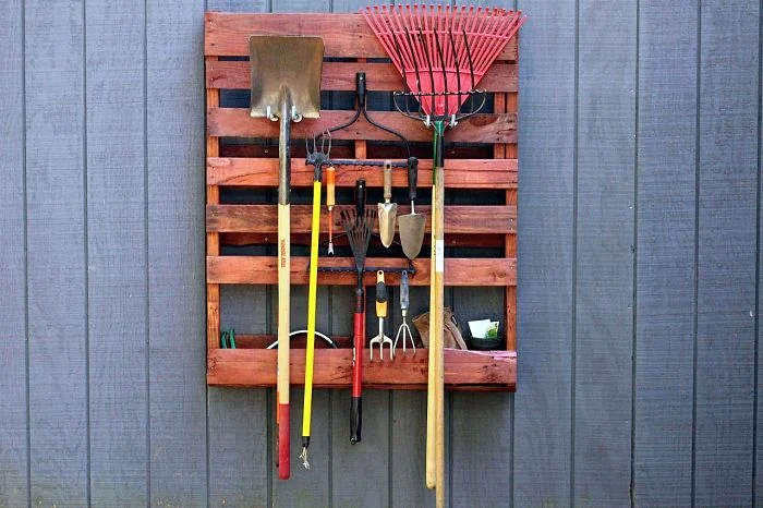 Palet de madera colgado de la pared con palas, rastrillo y herramientas de jardín
