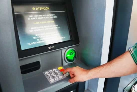 Mano pulsando el teclado de un cajero automático con un aviso de atención en pantalla