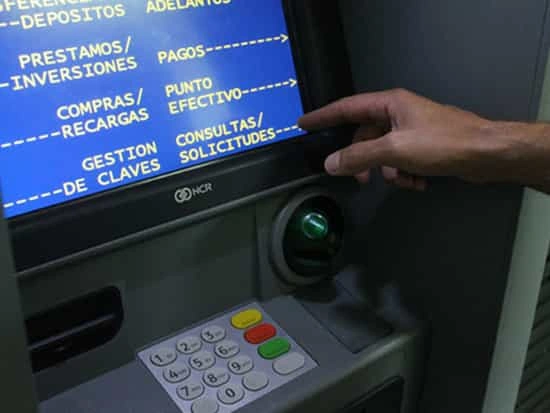 Mano señala las opciones de la pantalla de un cajero, sobre el teclado y la ranura de tarjetas