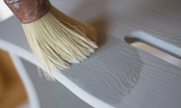 Brocha de cerdas claras pintando de gris con chalk paint una pieza de madera