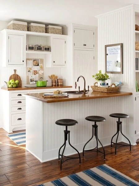 Cocina pequeña de estilo rústico en blanco con barra de madera, taburetes metálicos y muebles con almacenamiento.