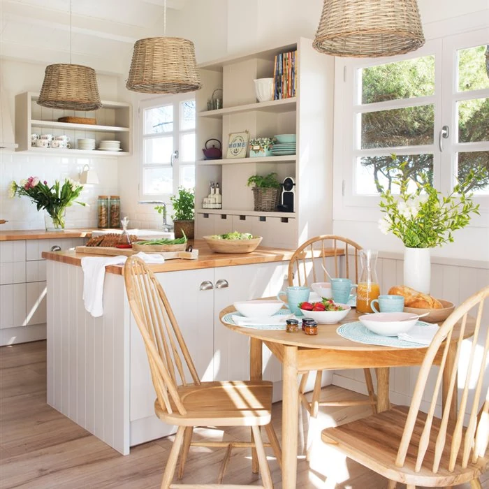 Cocina comedor de estilo rústico moderno, con gabinetes blancos, encimera de madera y lámparas de mimbre, creando un ambiente luminoso y acogedor.