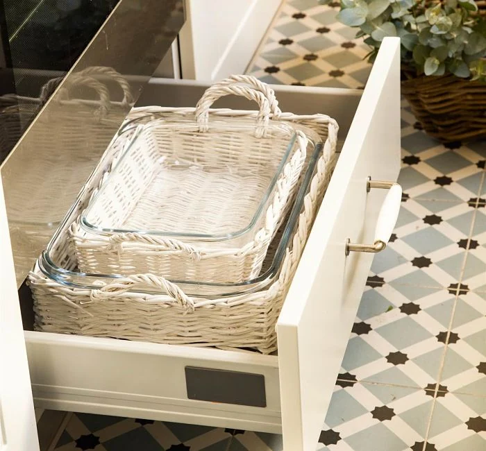 Cajón de cocina, usando cestas de mimbre blancas para almacenar fuentes de cristal y mantener el orden.