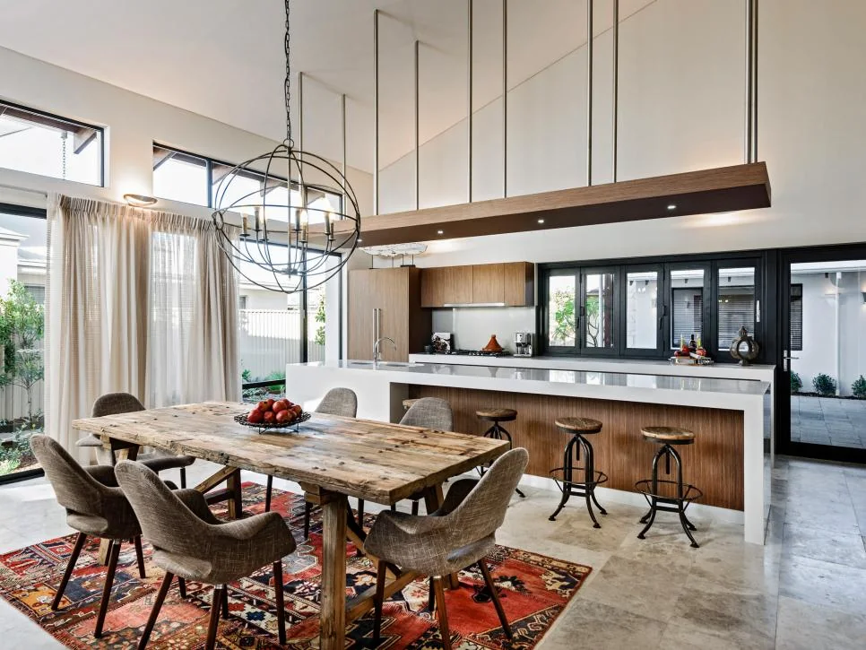 Cocina comedor de lujo con espacio abierto, destacando una mesa rústica de madera, isla moderna y una gran lámpara de esfera industrial.