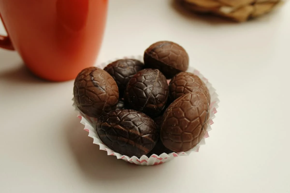 Varios huevitos de chocolate de Pascua macizos, con un patrón en relieve, servidos en un capacillo de papel junto a una taza.