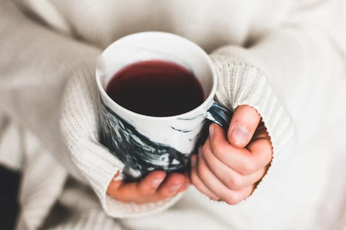 Persona con suéter blanco sosteniendo una taza de té caliente