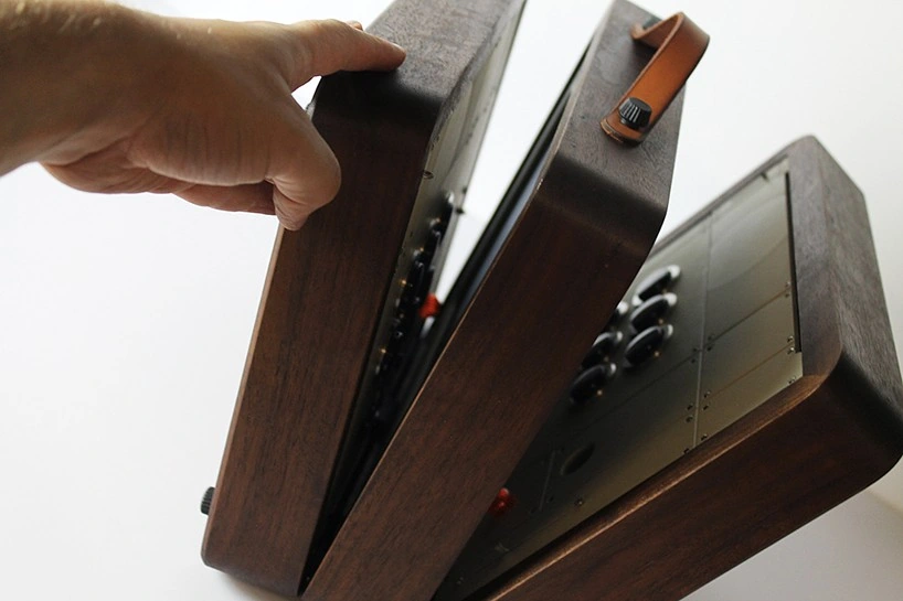 Una mano abre las tapas de una consola portátil de madera con asa de cuero
