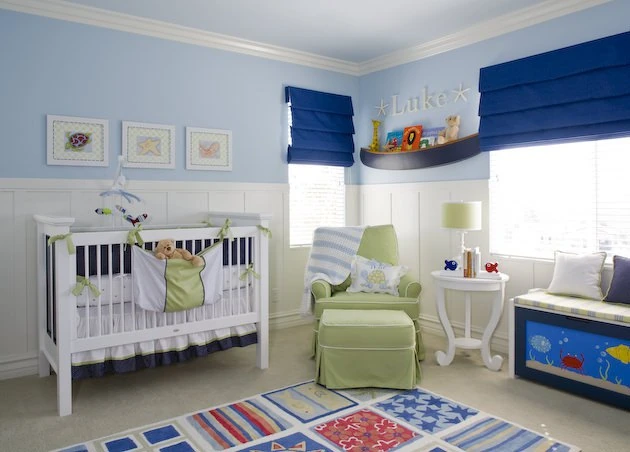 Habitación de bebé para niño con temática marina, paredes azules, cuna blanca y un sillón mecedor verde para lactancia.