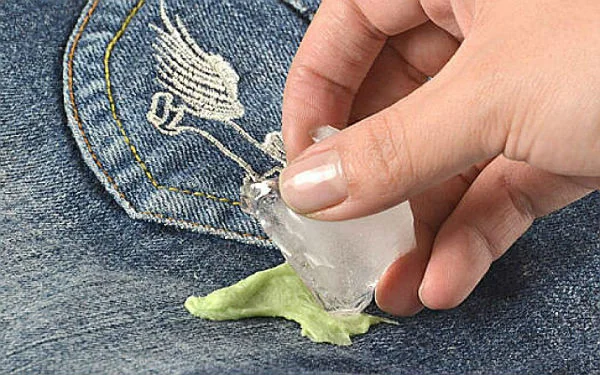 Quitar chicle de una prenda de jean es fácil con hielo o metiendo la prenda en freezer. jean con goma de mascar pegada y una mujer intentando quitar el chicle con un hielo