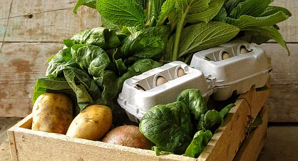 Caja de madera con vegetales frescos, papas, espinaca y huevos orgánicos, símbolo de consumo responsable y alimentación sostenible.