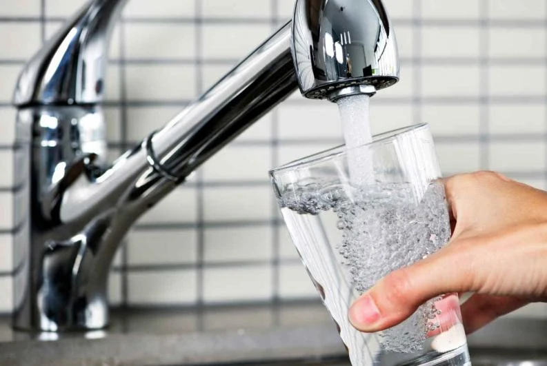 Mano llenando un vaso con agua potable del grifo, símbolo de consumo responsable y hábitos sostenibles.
